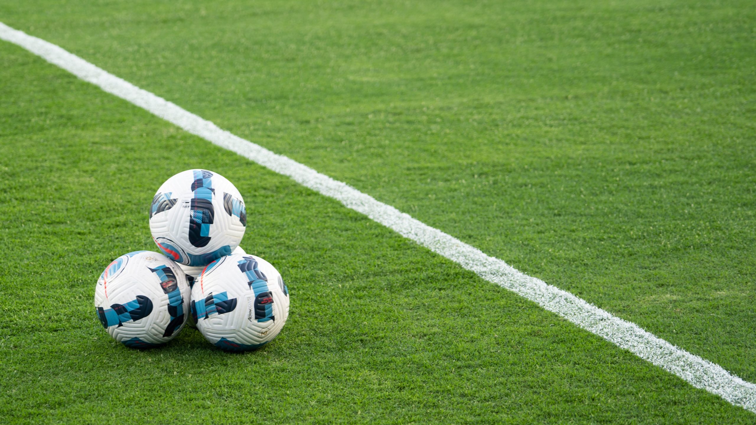 A pyramid shape of four soccer balls next to a white line of a soccer pitch.